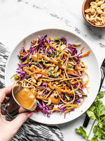 Cold peanut noodle salad with peanut sauce being drizzled over top